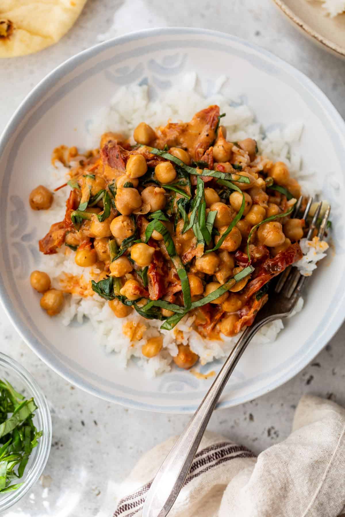 A plate of rice topped with chickpeas in a tomato-based sauce and garnished with fresh herbs, with a fork on the side.