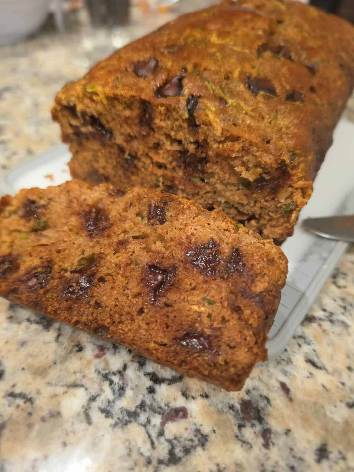 Sliced loaf of zucchini bread with visible chocolate chips on a speckled countertop.