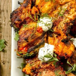 Grilled harissa chicken garnished with fresh herbs and dollops of creamy white sauce on a white plate.