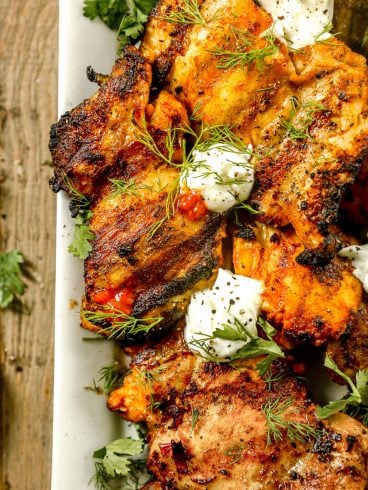 Grilled harissa chicken garnished with fresh herbs and dollops of creamy white sauce on a white plate.