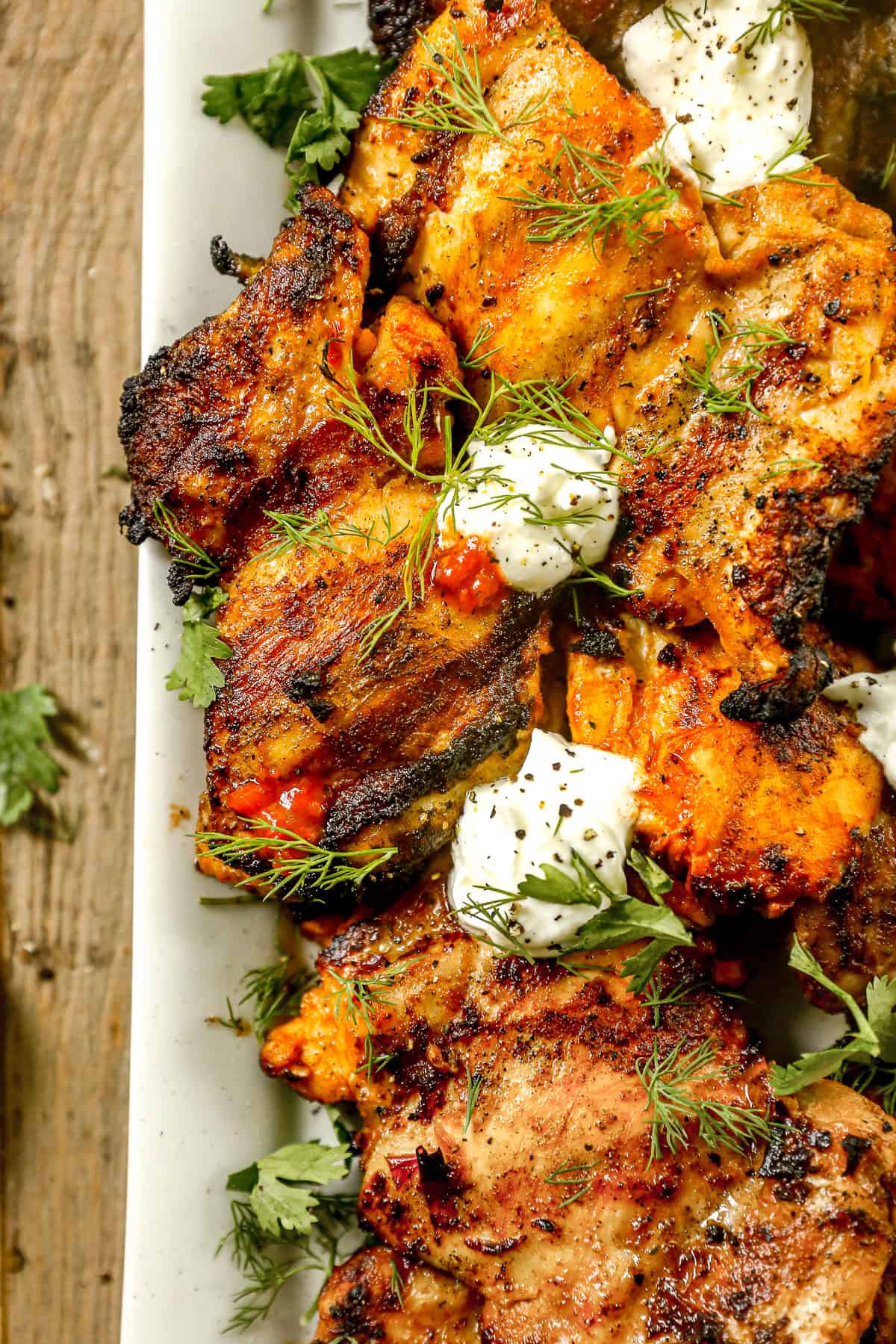 Grilled harissa chicken garnished with fresh herbs and dollops of creamy white sauce on a white plate.
