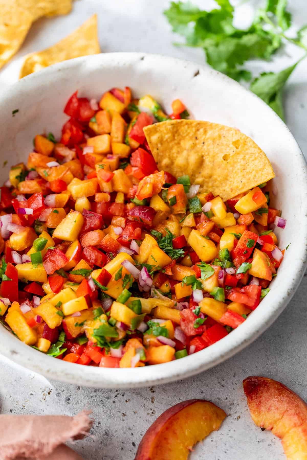 A bowl of peach salsa with diced tomatoes, onions, cilantro, and a tortilla chip dipped inside.