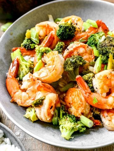 Shrimp stir-fry with broccoli and green onions served in a gray bowl on a wooden table.