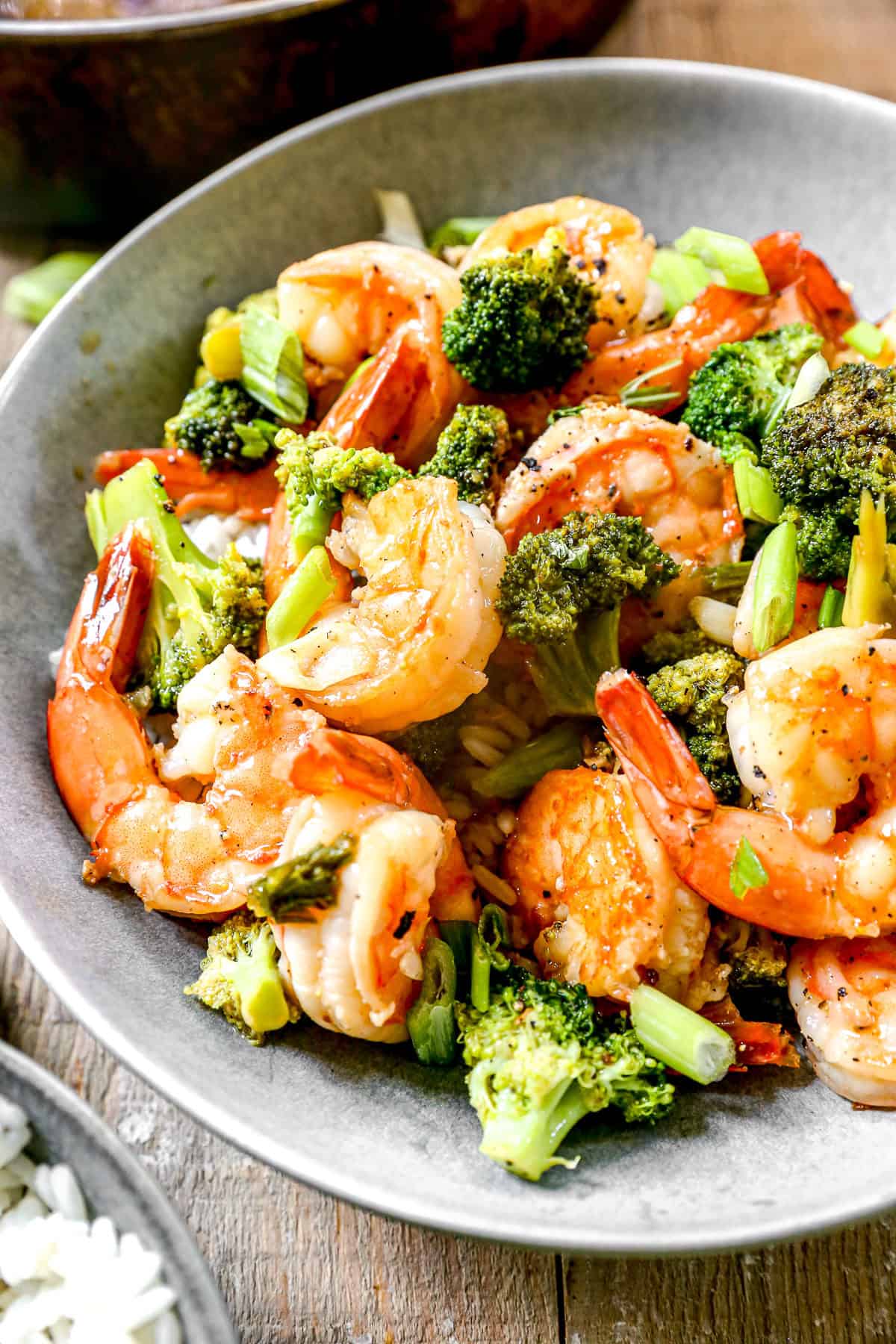 Shrimp stir-fry with broccoli and green onions served in a gray bowl on a wooden table.
