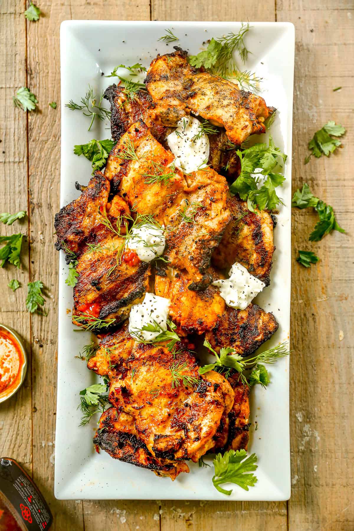 Grilled harissa chicken pieces garnished with fresh herbs and dollops of sauce on a white rectangular plate.