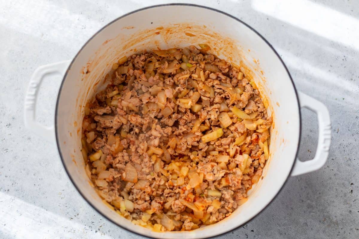 Cooked ground meat and chopped onions in a white pot on a light countertop, illuminated by natural light.
