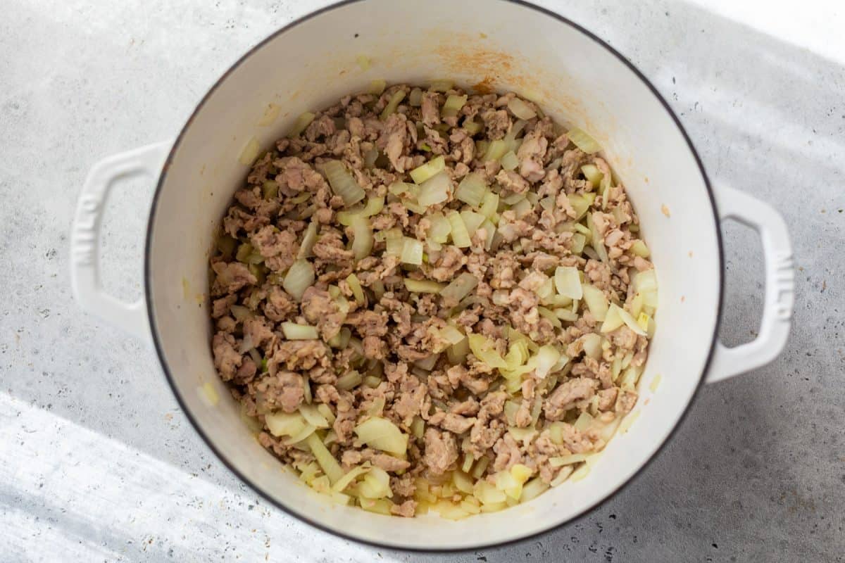 Cooked ground meat and chopped onions in a white pot on a light-colored surface.