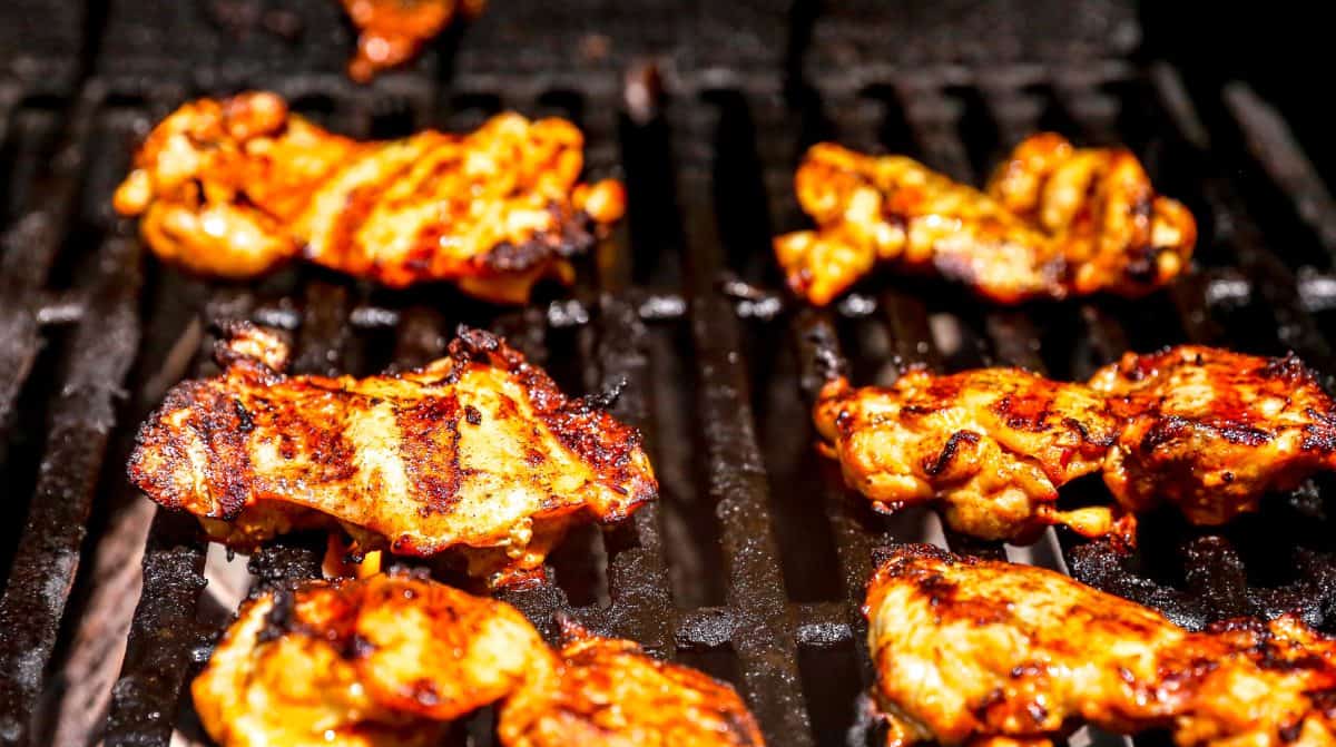 Pieces of harissa chicken being grilled on a barbecue with visible grill marks and charred edges.