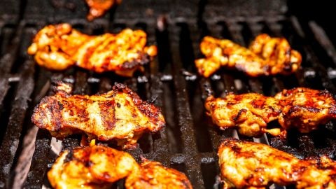 Pieces of harissa chicken being grilled on a barbecue with visible grill marks and charred edges.