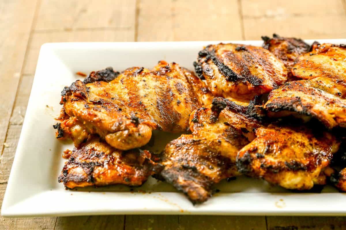 Grilled harissa chicken thighs arranged on a rectangular white plate atop a wooden surface.