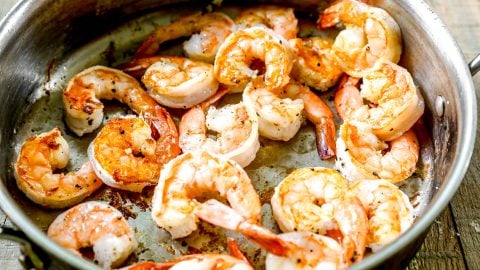 Cooked shrimp sizzling in a metal skillet on a wooden surface.