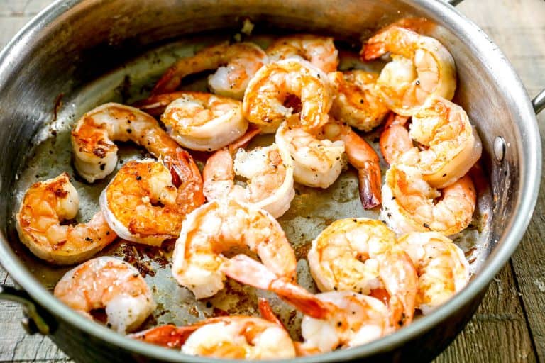 Cooked shrimp sizzling in a metal skillet on a wooden surface.