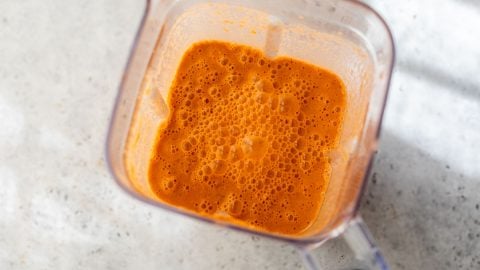 Watermelon gazpacho mixture with bubbles in a blender on a light, speckled countertop.