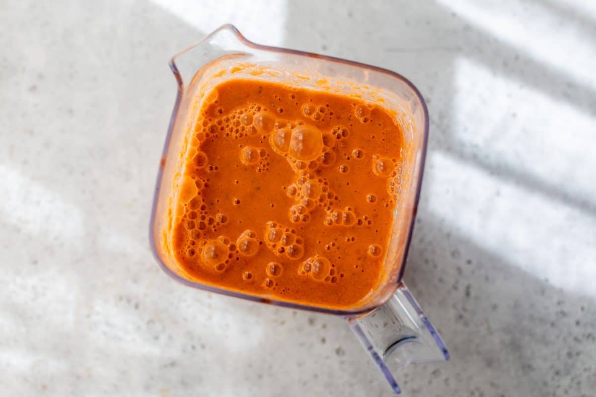 A clear blender filled with watermelon gazpacho sits on a light, speckled countertop.