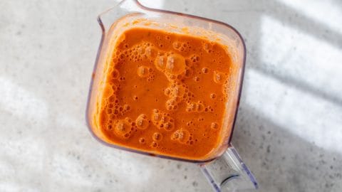 A clear blender filled with watermelon gazpacho sits on a light, speckled countertop.