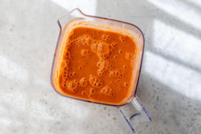A clear blender filled with watermelon gazpacho sits on a light, speckled countertop.