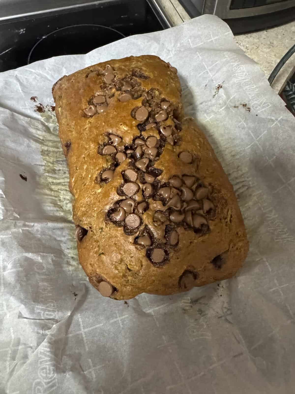 A loaf of banana bread topped with chocolate chips rests on parchment paper on a kitchen counter.