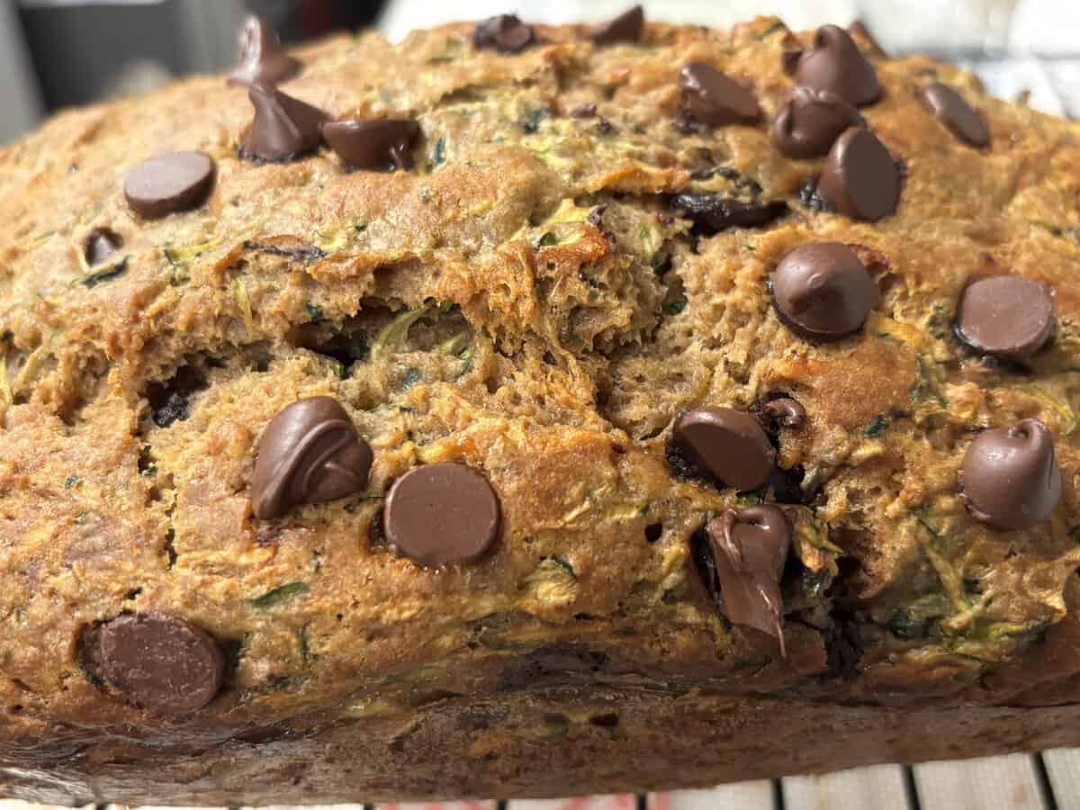 Close-up of a loaf of zucchini bread topped with melted and unmelted chocolate chips, cooling on a wire rack.