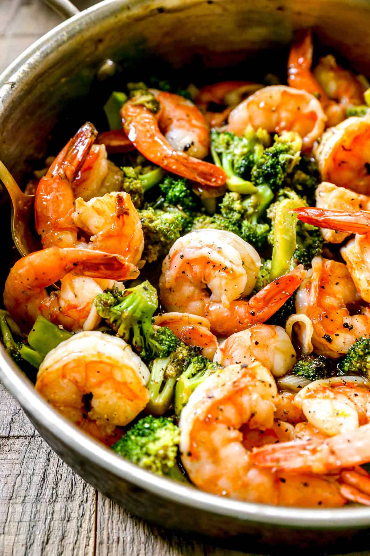 Shrimp and broccoli cooked in a skillet, seasoned with pepper, on a wooden surface.