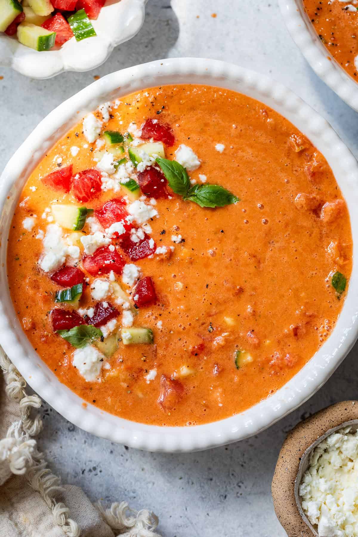 A bowl of creamy watermelon gazpacho topped with diced tomatoes, cucumbers, feta cheese, and fresh herbs.