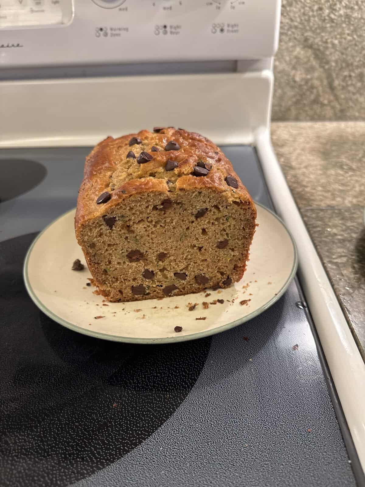 A loaf of banana bread with chocolate chips sits sliced open on a plate atop a stove.