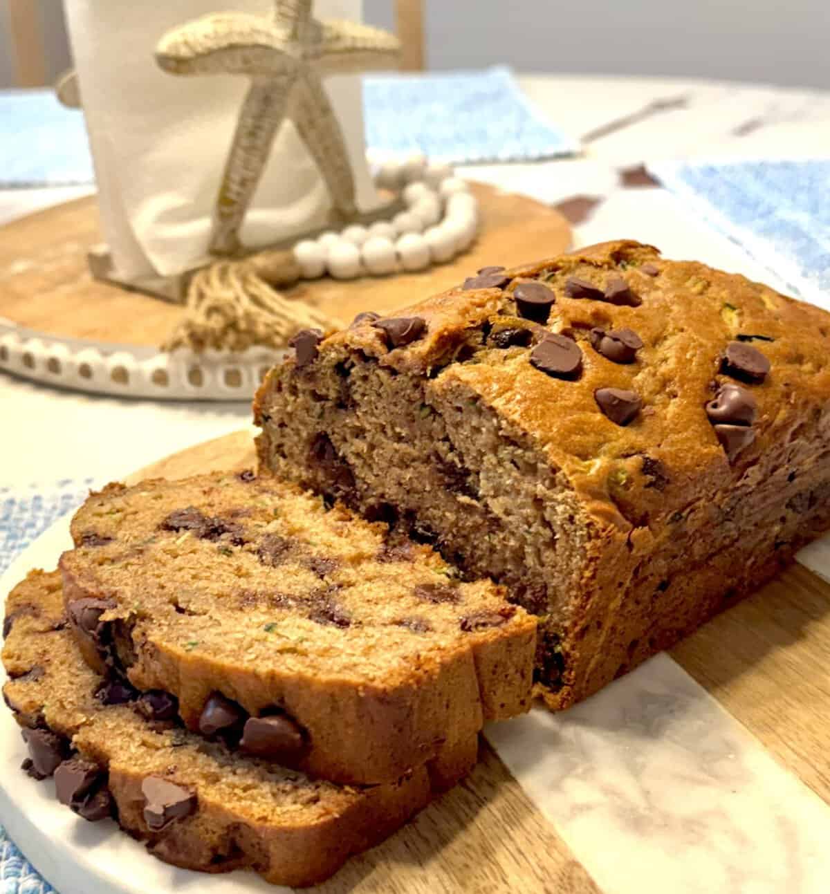 Sliced chocolate chip zucchini bread on a marble cutting board, with a beach-themed napkin holder in the background.