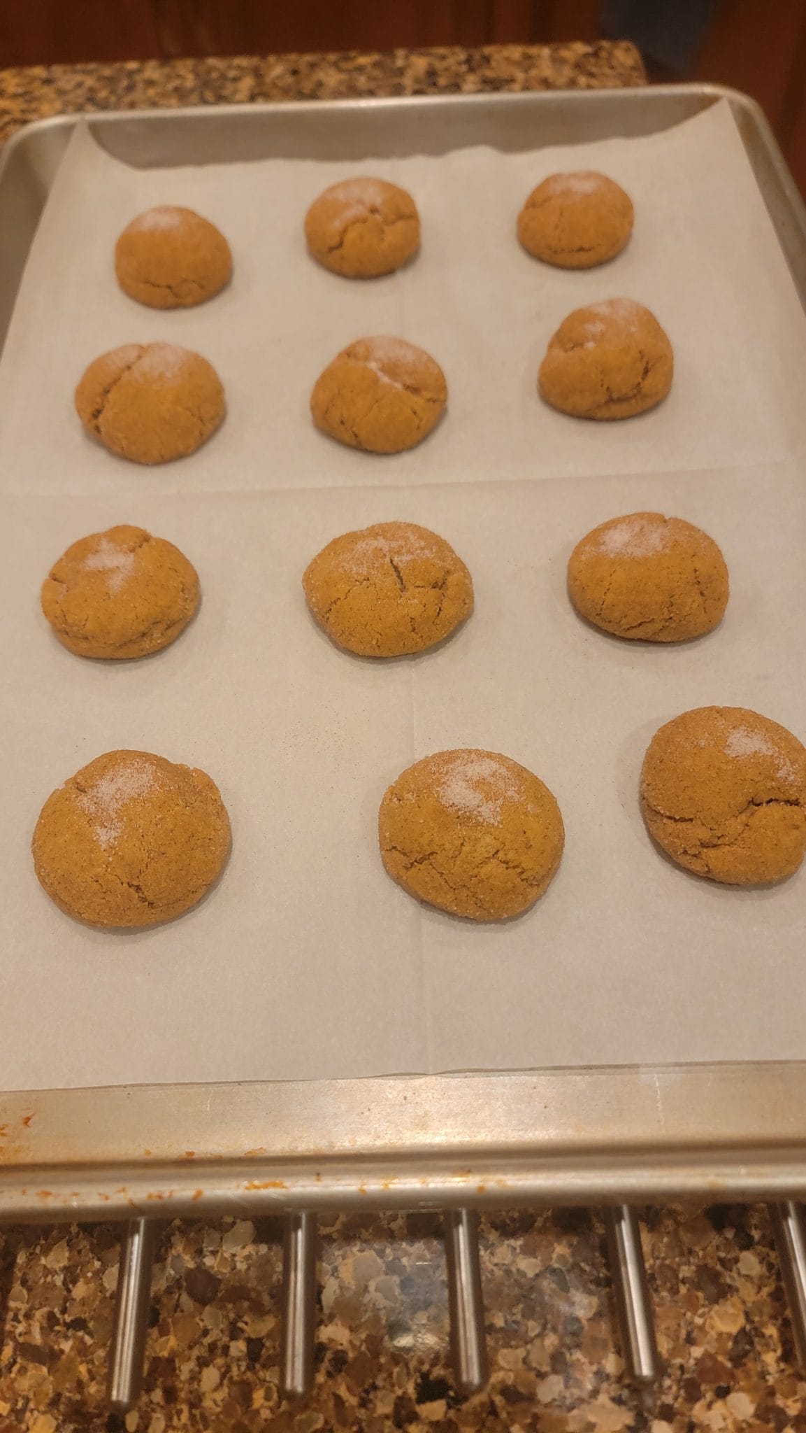 Twelve sugar-dusted cookies on parchment paper, arranged in rows on a metal baking sheet.