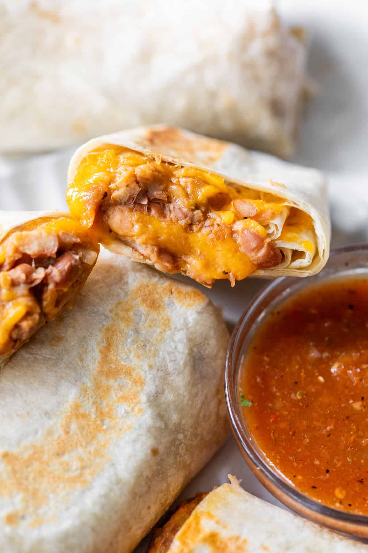 A bean and cheese burrito cut in half shows beans and melted cheese, served with a small bowl of red salsa.