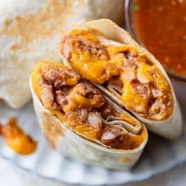 A bean and cheese burrito cut in half, filled with beans and melted cheese, next to a bowl of red salsa and a sprig of cilantro.