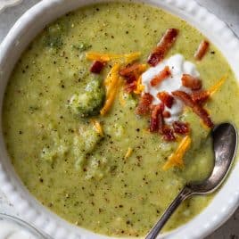 Creamy broccoli potato soup topped with shredded cheese, bacon bits, and a dollop of sour cream in a white bowl with a spoon.