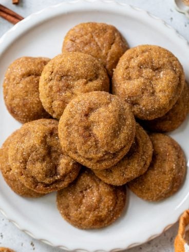 A plate of round, sugar-coated pumpkin spice cookies arranged in a pile on a white plate.