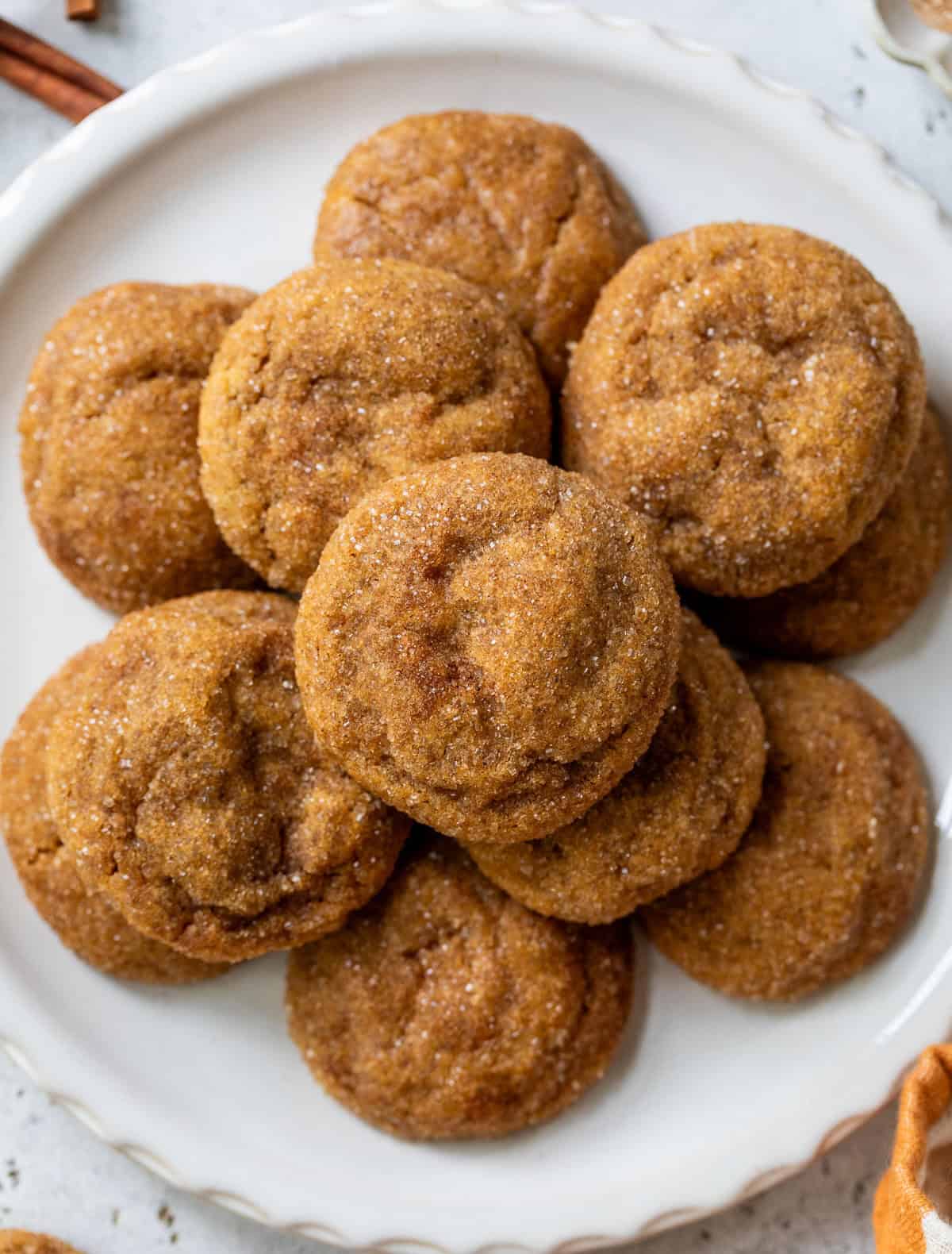 A plate of round, sugar-coated pumpkin spice cookies arranged in a pile on a white plate.
