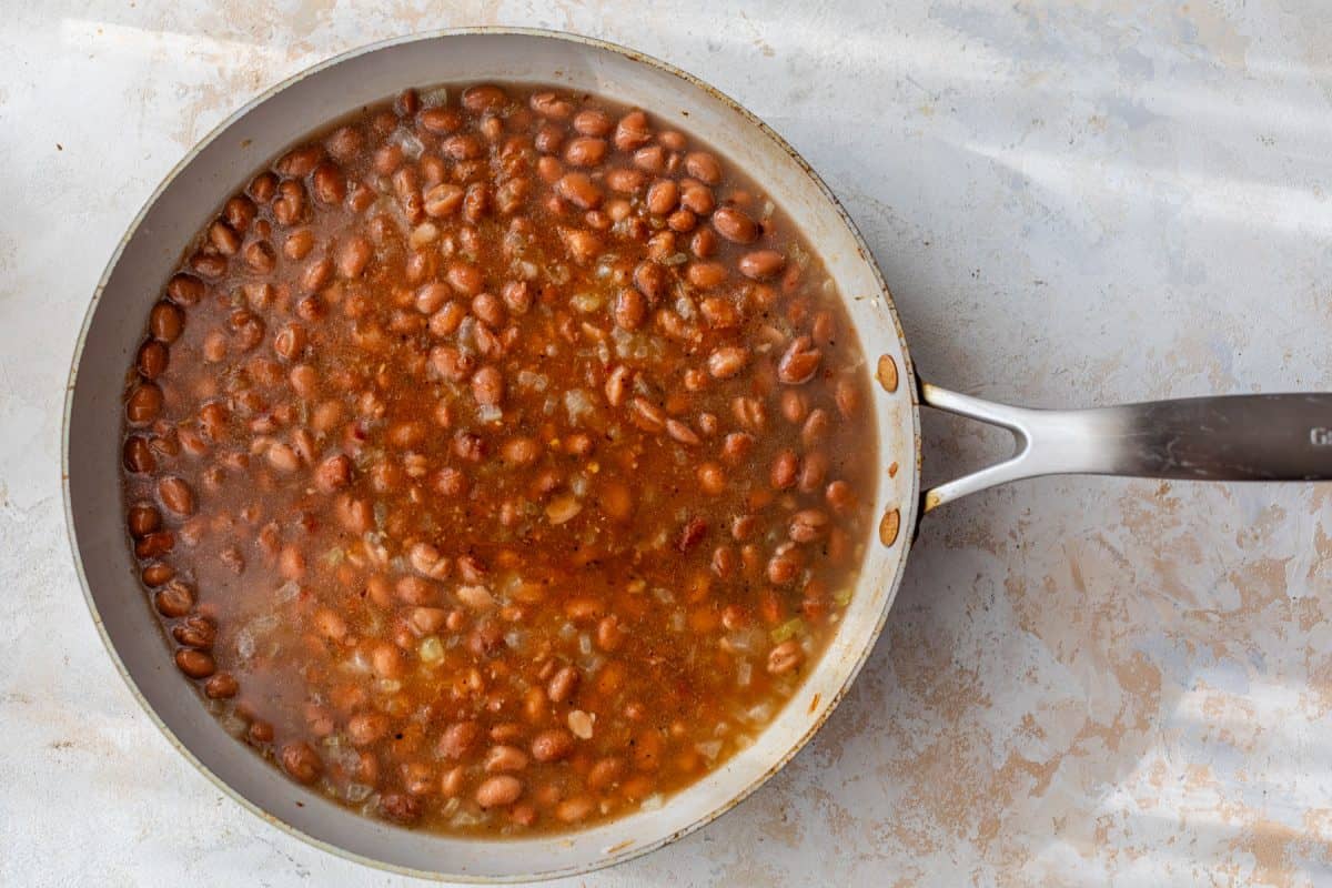 A skillet filled with pinto beans simmering in a seasoned, reddish-brown broth.