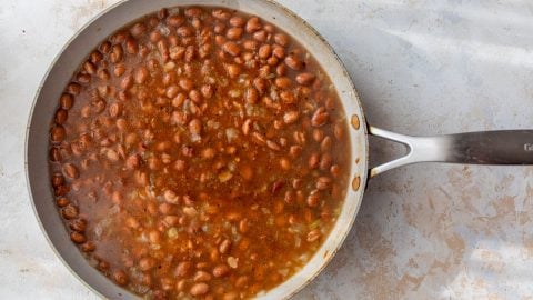 A skillet filled with pinto beans simmering in a seasoned, reddish-brown broth.