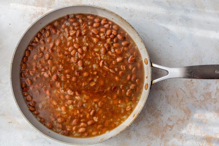 A skillet filled with pinto beans simmering in a seasoned, reddish-brown broth.