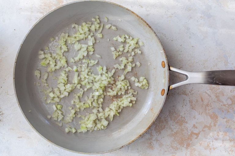 Diced onions cooking in a large silver skillet on a light-colored countertop.