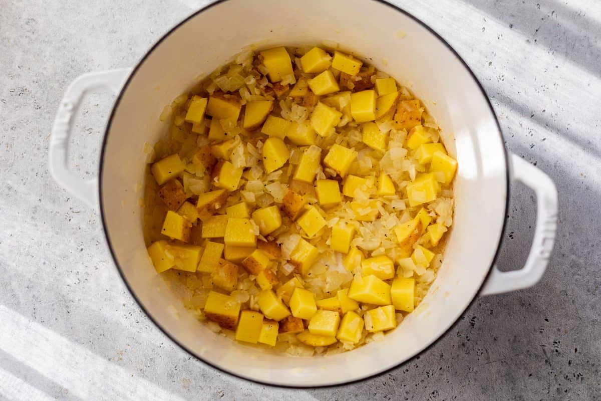 Diced potatoes and onions cooking in a white pot on a gray countertop, with sunlight casting shadows.