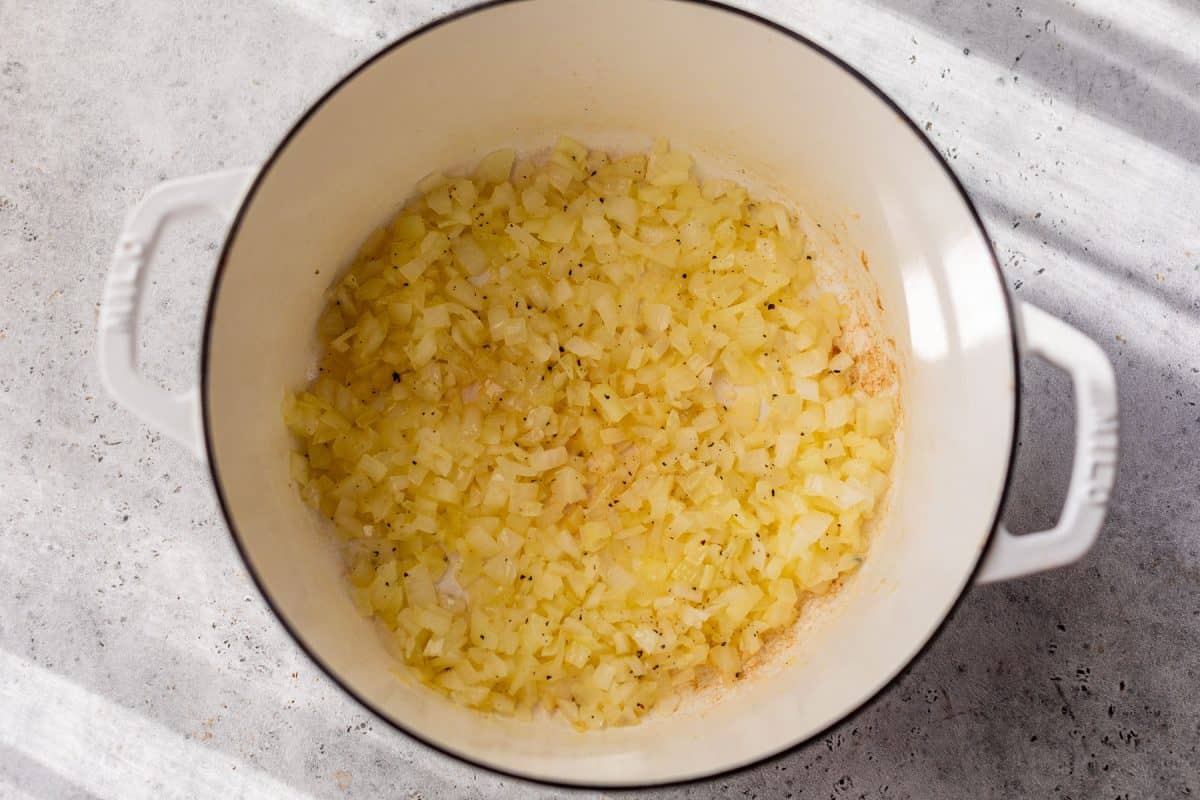 Diced onions sautéing in a white Dutch oven on a light gray countertop, with some browning visible.
