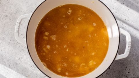 A white pot filled with broth and chopped onions sits on a light gray countertop in sunlight.