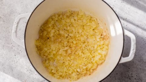 Diced onions sautéing in a white Dutch oven on a light gray countertop, with some browning visible.