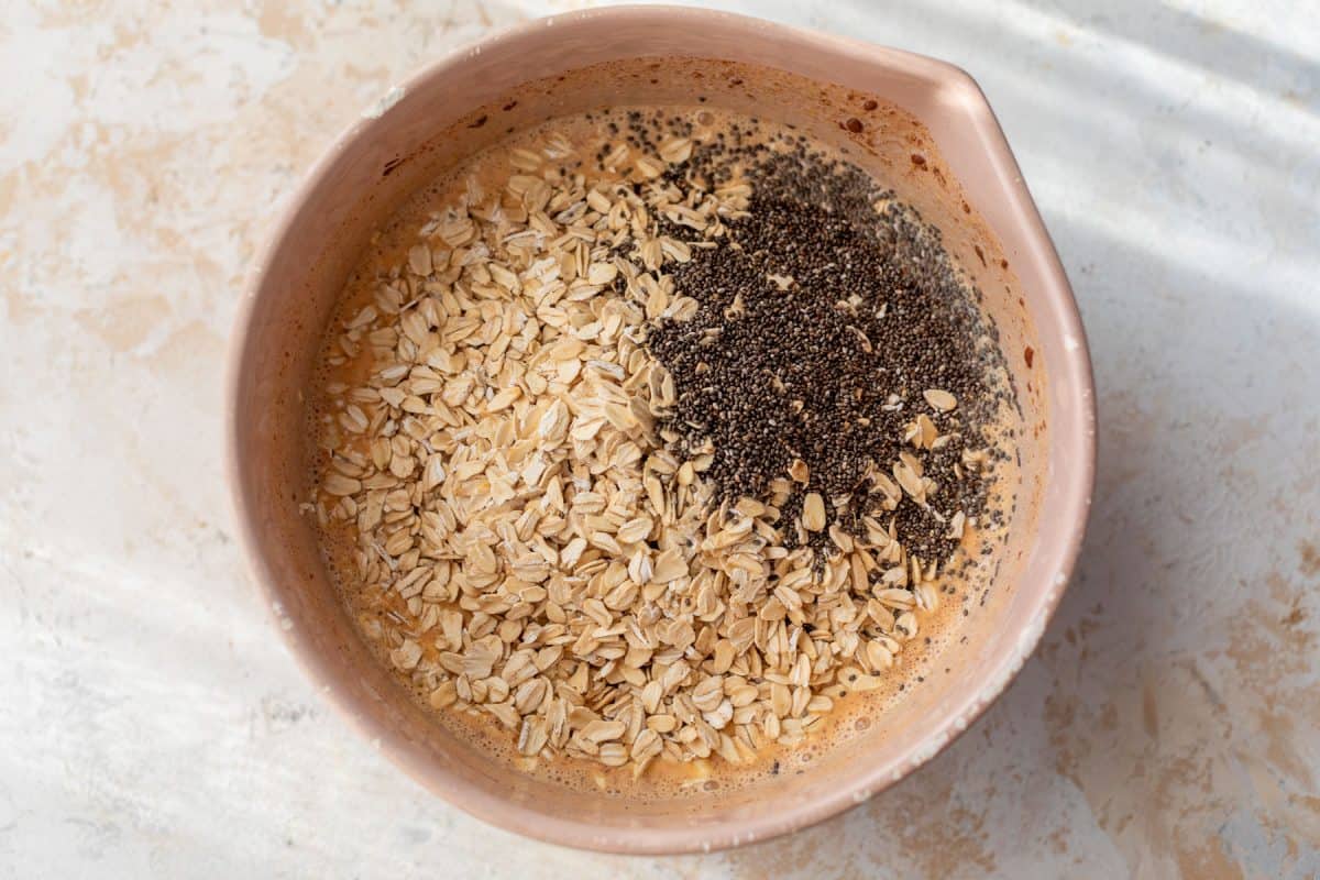 A mixing bowl with oats, chia seeds, and liquid ingredients before being stirred together.