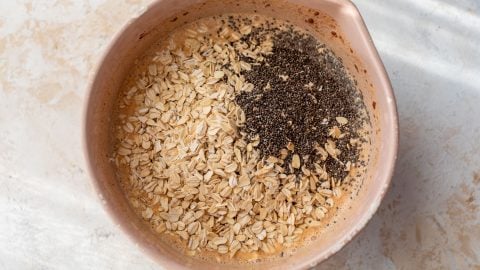 A mixing bowl with oats, chia seeds, and liquid ingredients before being stirred together.