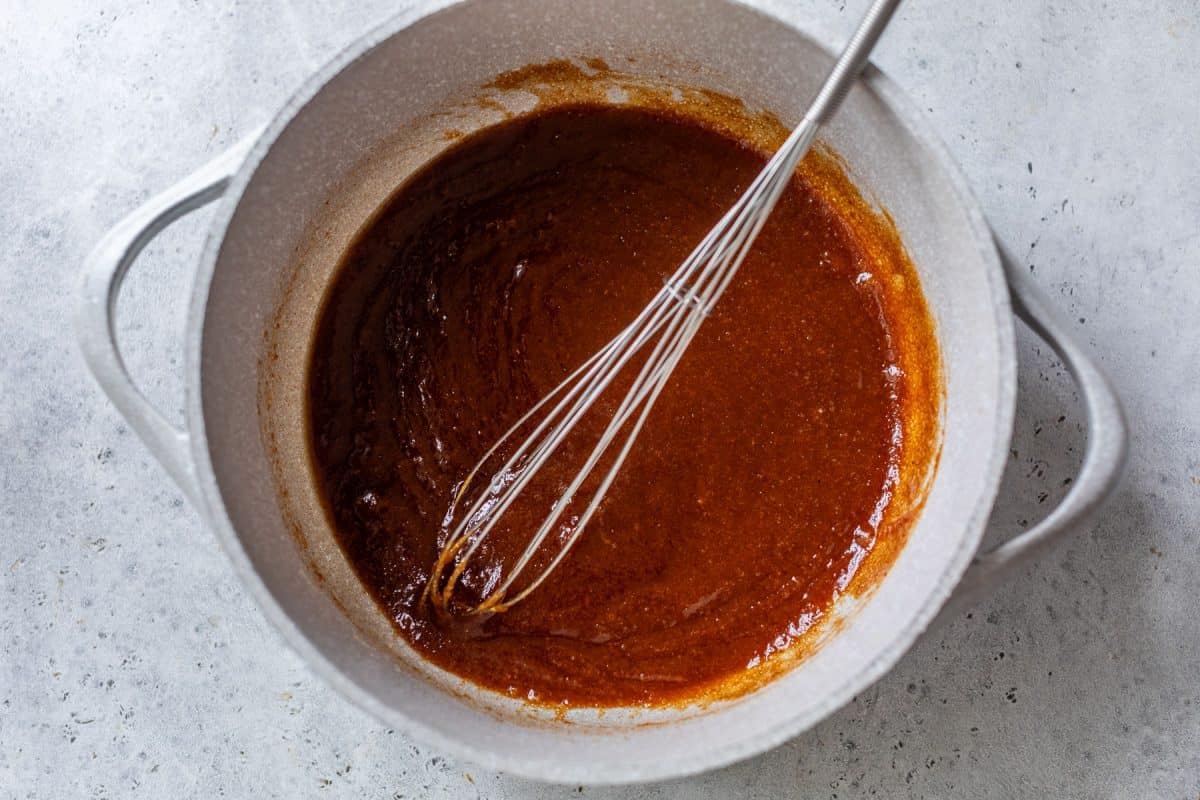 A whisk stirring thick pumpkin mixture in a white pot on a light gray countertop.