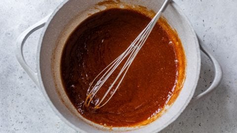 A whisk stirring thick pumpkin mixture in a white pot on a light gray countertop.