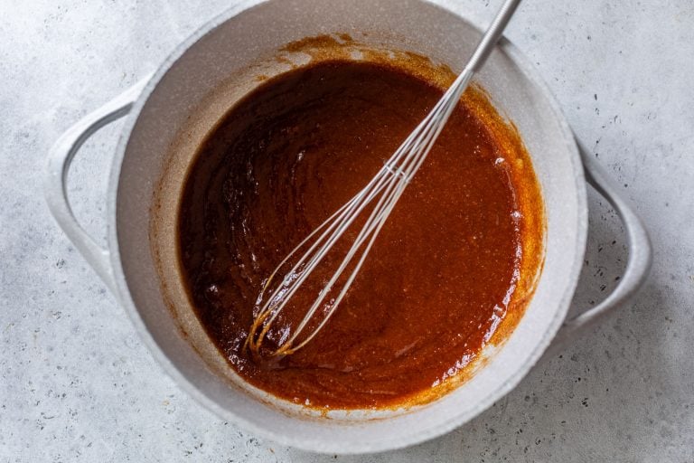 A whisk stirring thick pumpkin mixture in a white pot on a light gray countertop.