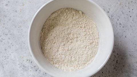 A white bowl filled with flour sits on a light gray textured surface.