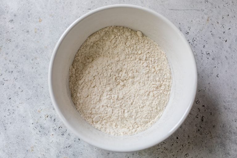 A white bowl filled with flour sits on a light gray textured surface.