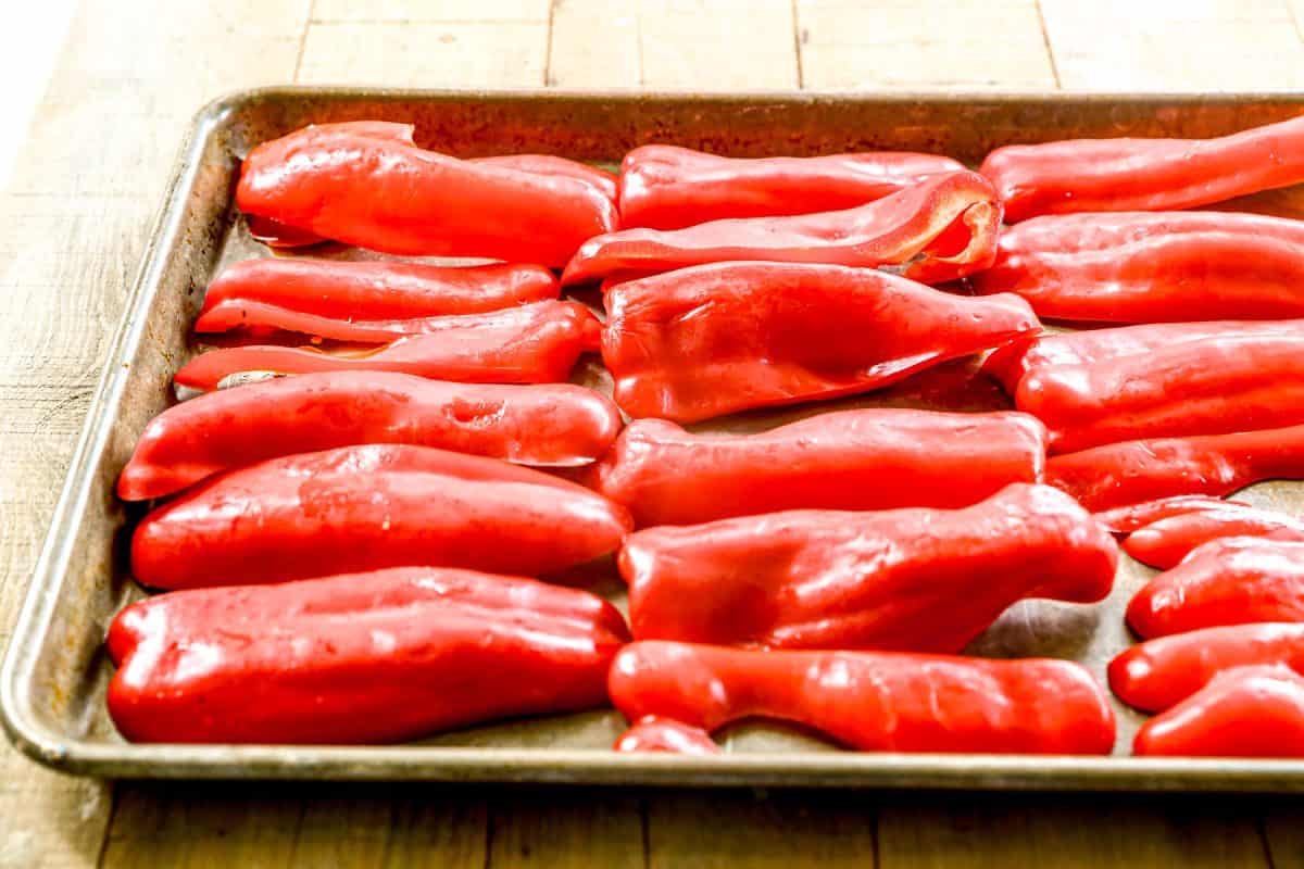 Halved red bell peppers arranged on a baking sheet, ready to be roasted, on a wooden surface.