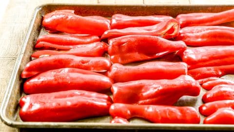 Halved red bell peppers arranged on a baking sheet, ready to be roasted, on a wooden surface.