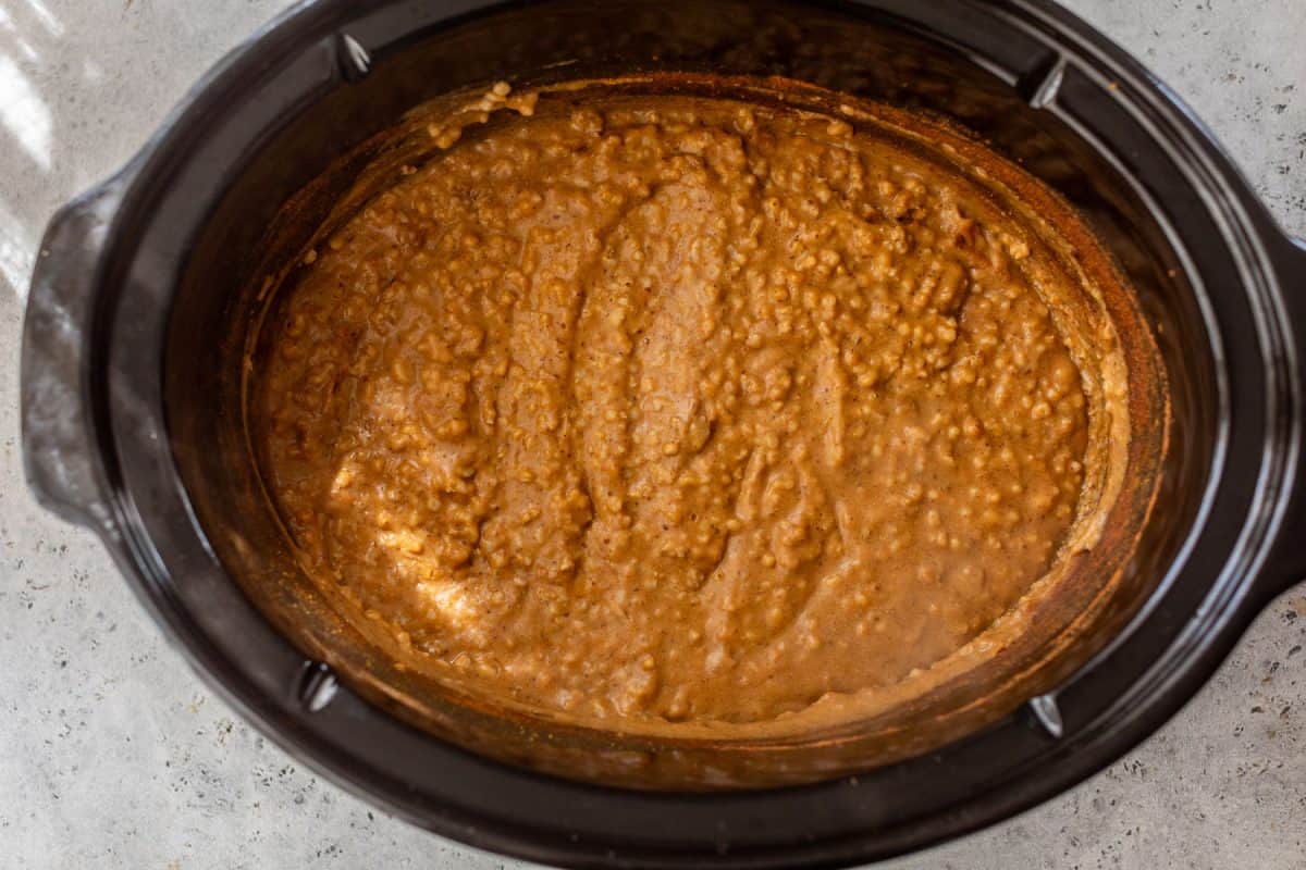Pumpkin oatmeal mixture cooking in a black slow cooker on a light countertop, viewed from above.